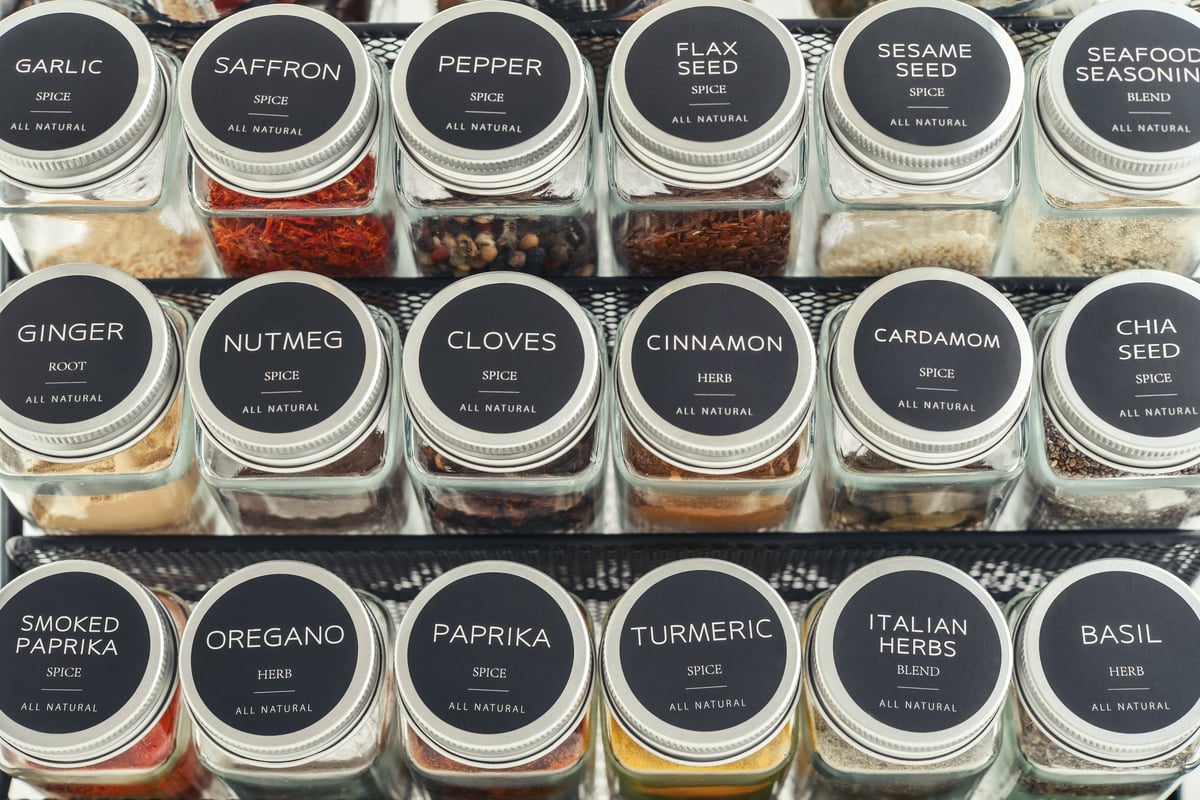 Assorted spices in glass jars with metal lids on a black metal shelf, closeup
