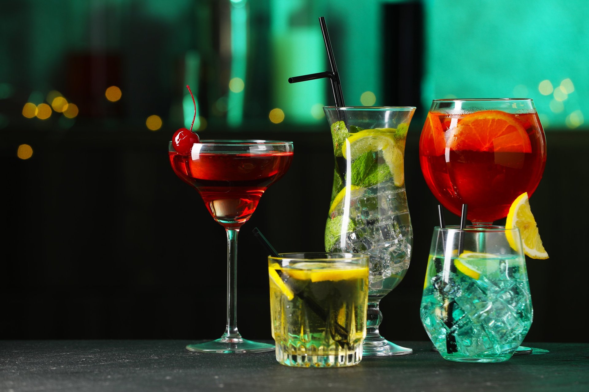 Glasses of tasty cocktails on dark table against blurred background with bokeh effect