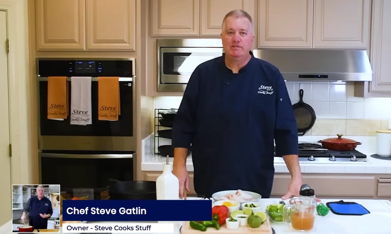 Chef Steve Gatlin standing in a modern kitchen with stainless steel appliances, fresh vegetables and ingredients on the counter in front of him