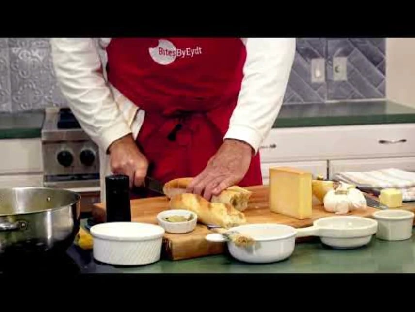 Chef in red apron grating cheese in kitchen with cooking ingredients and bowls on counter