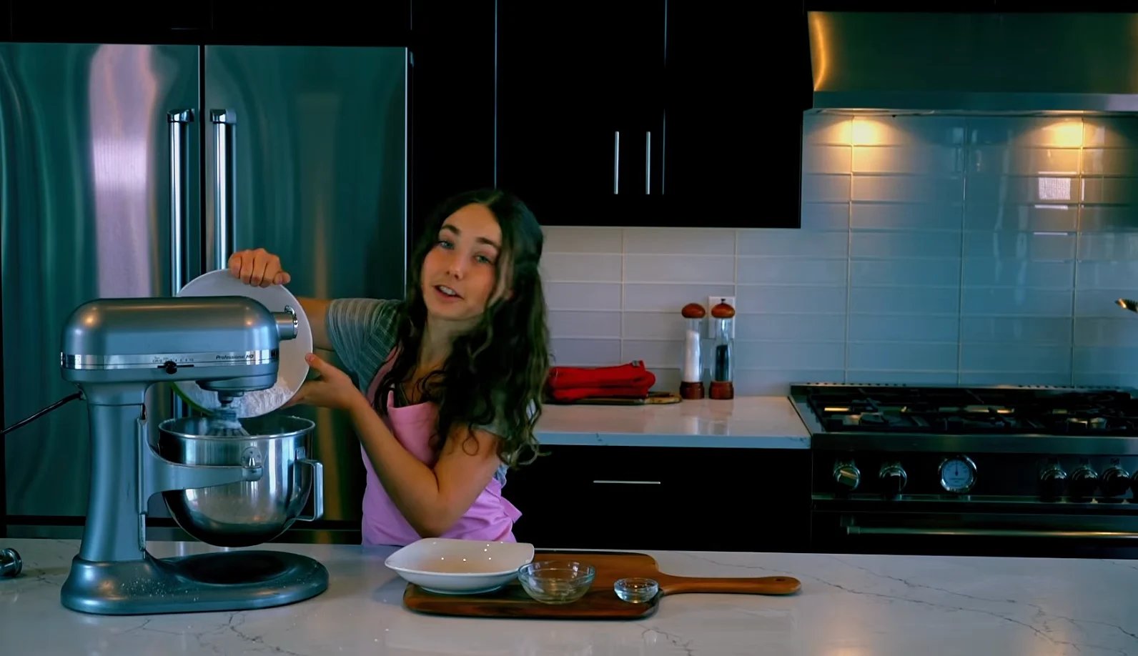 Woman using a stand mixer in a modern kitchen with teal cabinets and stainless steel appliances