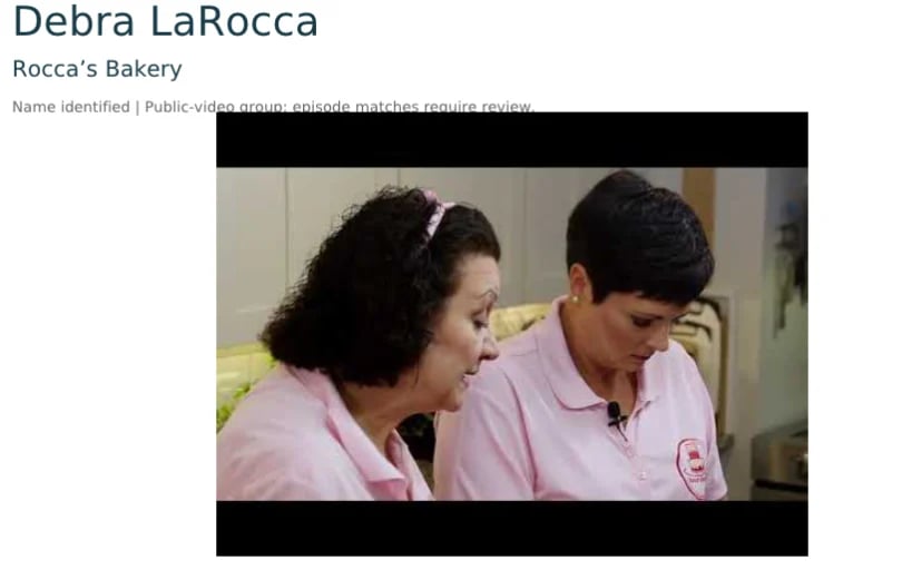 Debra LaRocca and another person wearing pink Roccas Bakery uniforms looking at something together