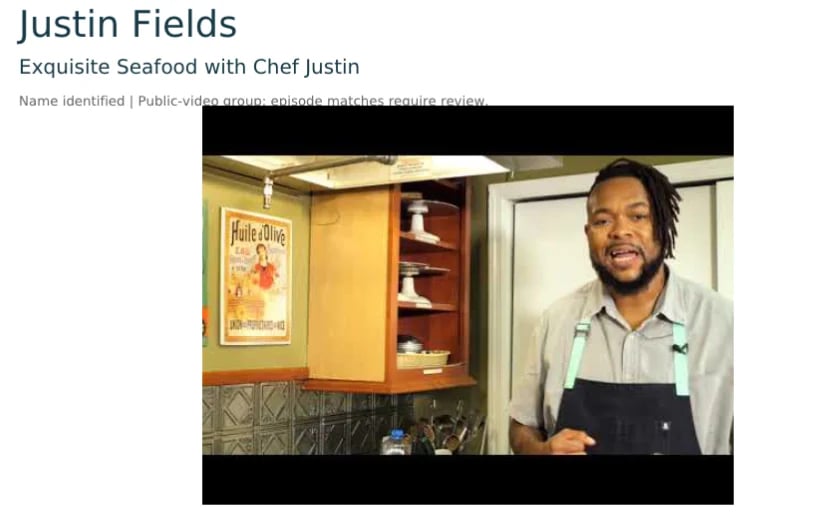 Chef Justin Fields in a kitchen wearing a white shirt and black apron, smiling at the camera with yellow cabinets visible behind him