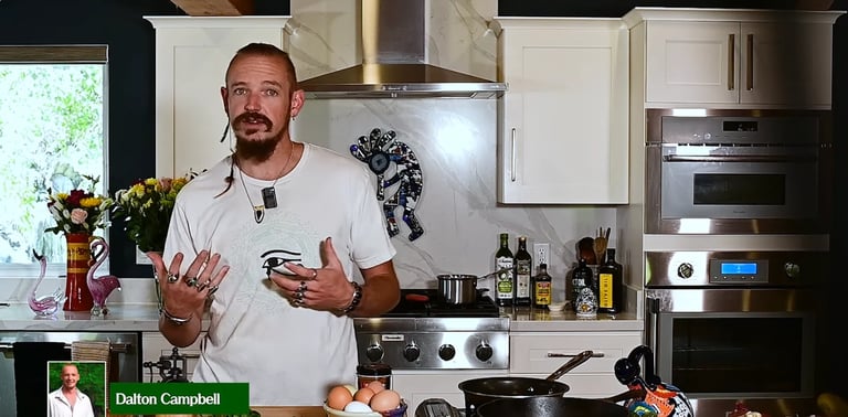 Man in white t-shirt gesturing while speaking in a modern kitchen with white cabinets and stainless steel appliances