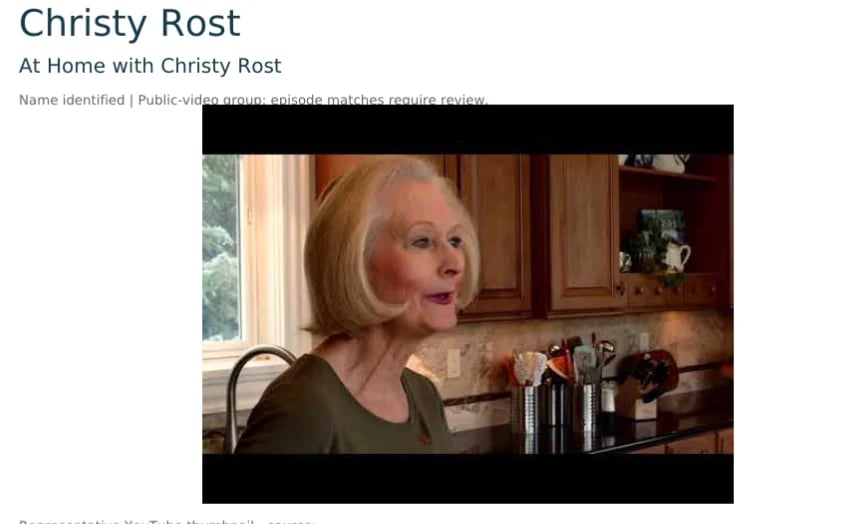 Christy Rost in her home kitchen, wearing a dark shirt, with wooden cabinets and windows visible in background