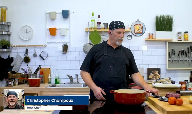 Chef Christopher Champoux in a professional kitchen with organized cookware and ingredients on white walls and shelves behind him.