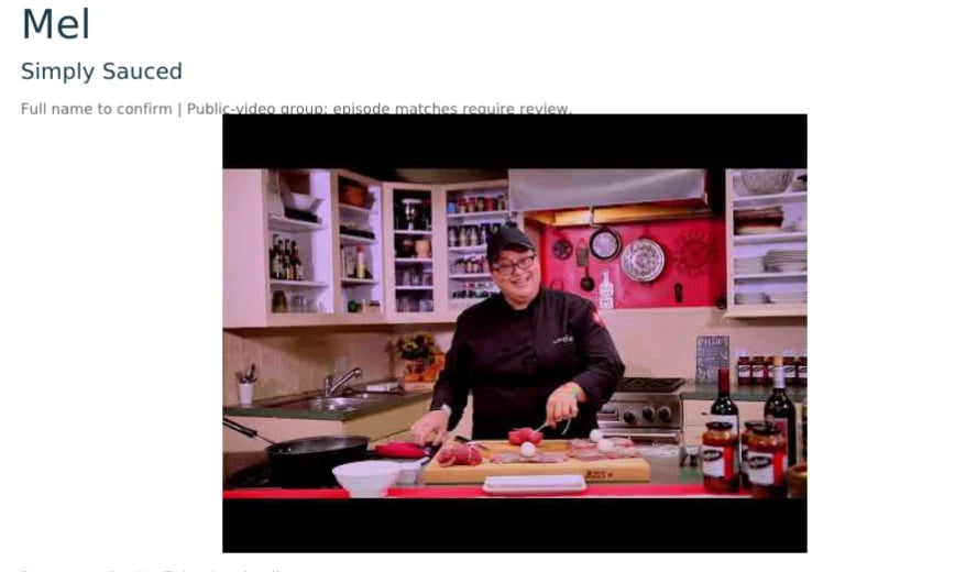 Woman in black chefs coat preparing food in a bright kitchen with shelves and bottles behind her