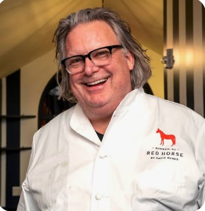 Man wearing glasses and white Red Horse branded polo shirt smiling at camera in indoor setting