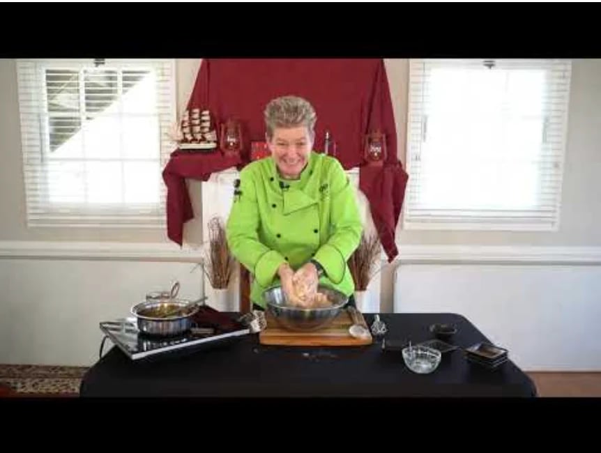 Older woman in bright green shirt cooking at black table with stove and kitchenware in a home setting