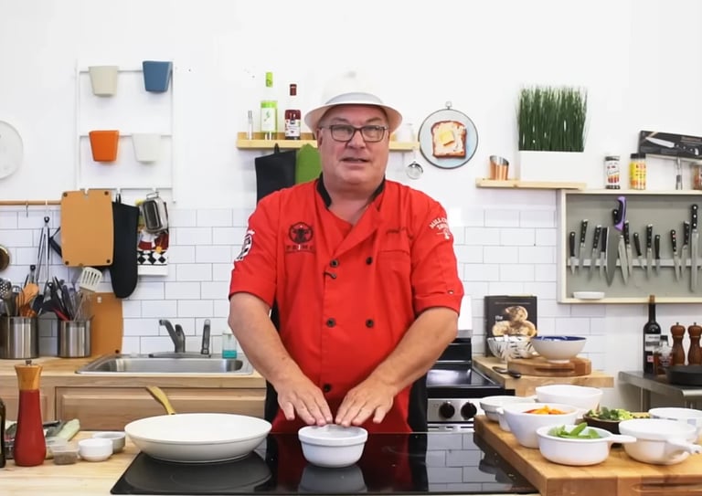 Chef Chris Perkey in red uniform and hat at kitchen counter demonstrating a cooking technique