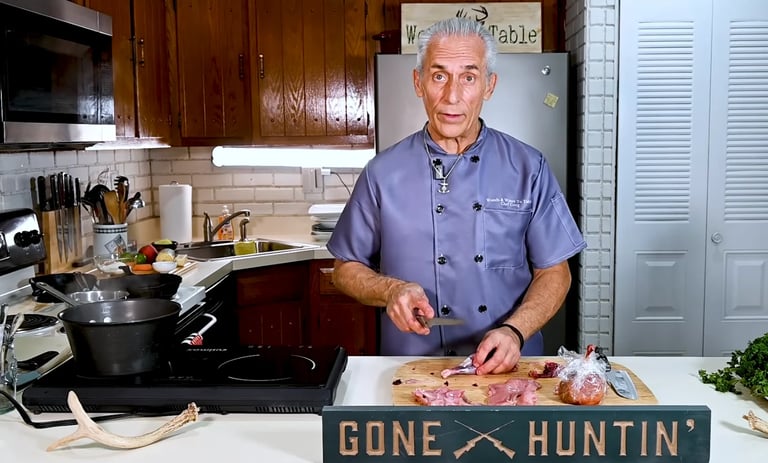 Older man in blue shirt preparing food in kitchen with a Gone Hunting sign on counter